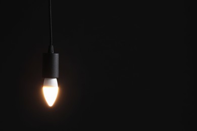 Photo of Glowing light bulb hanging on dark background. Space for text