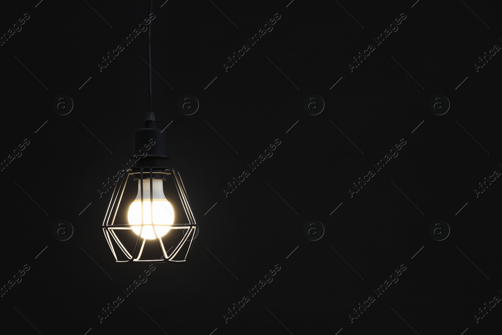 Photo of Chandelier with glowing light bulb hanging on dark background. Space for text