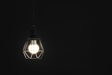 Photo of Chandelier with glowing light bulb hanging on dark background. Space for text