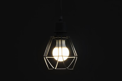 Photo of Chandelier with glowing light bulb hanging on dark background