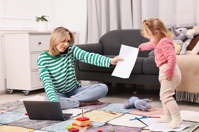 Photo of Work at home. Single mother talking by smartphone and her daughter on floor indoors