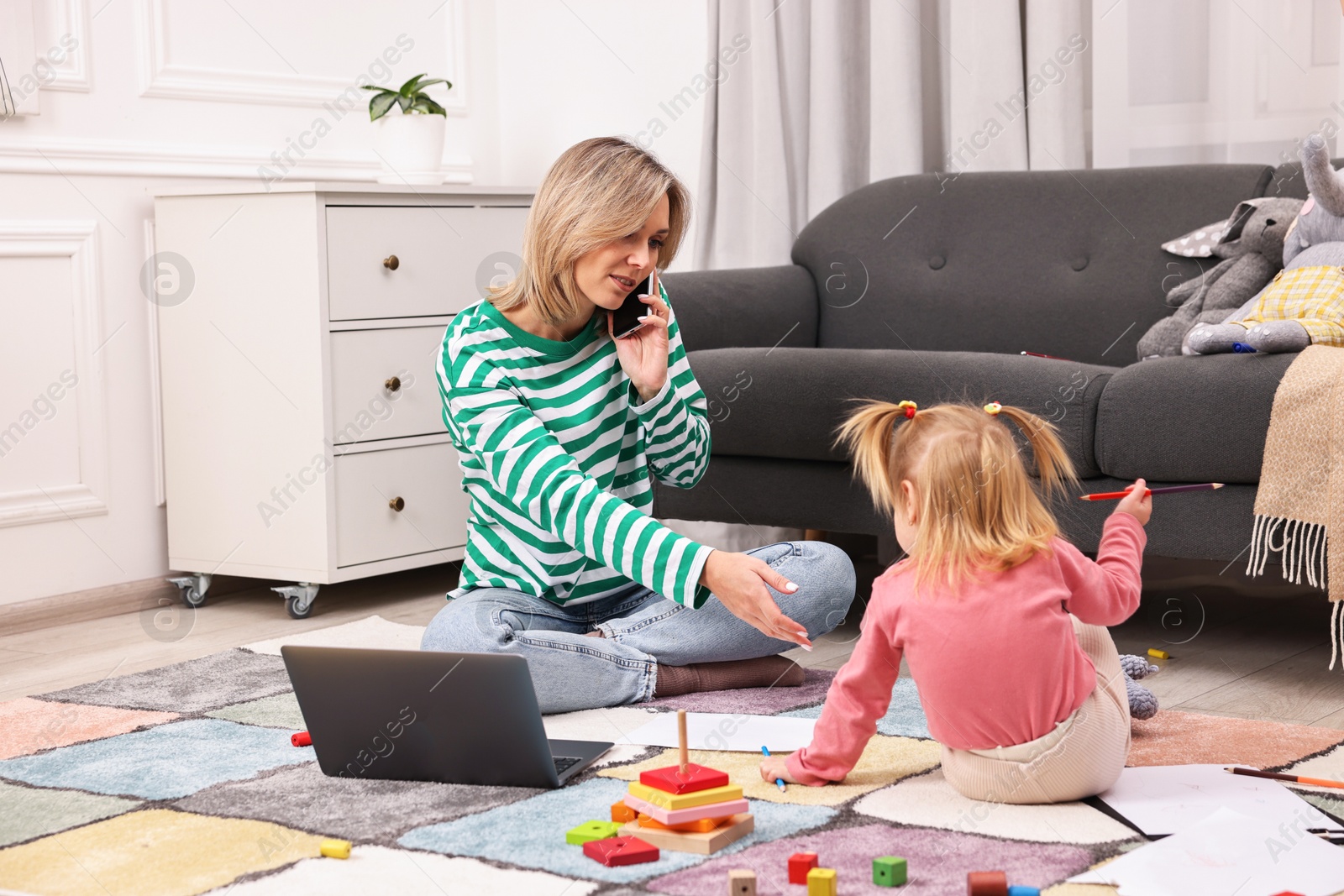 Photo of Work at home. Single mother talking by smartphone and her daughter drawing on floor indoors