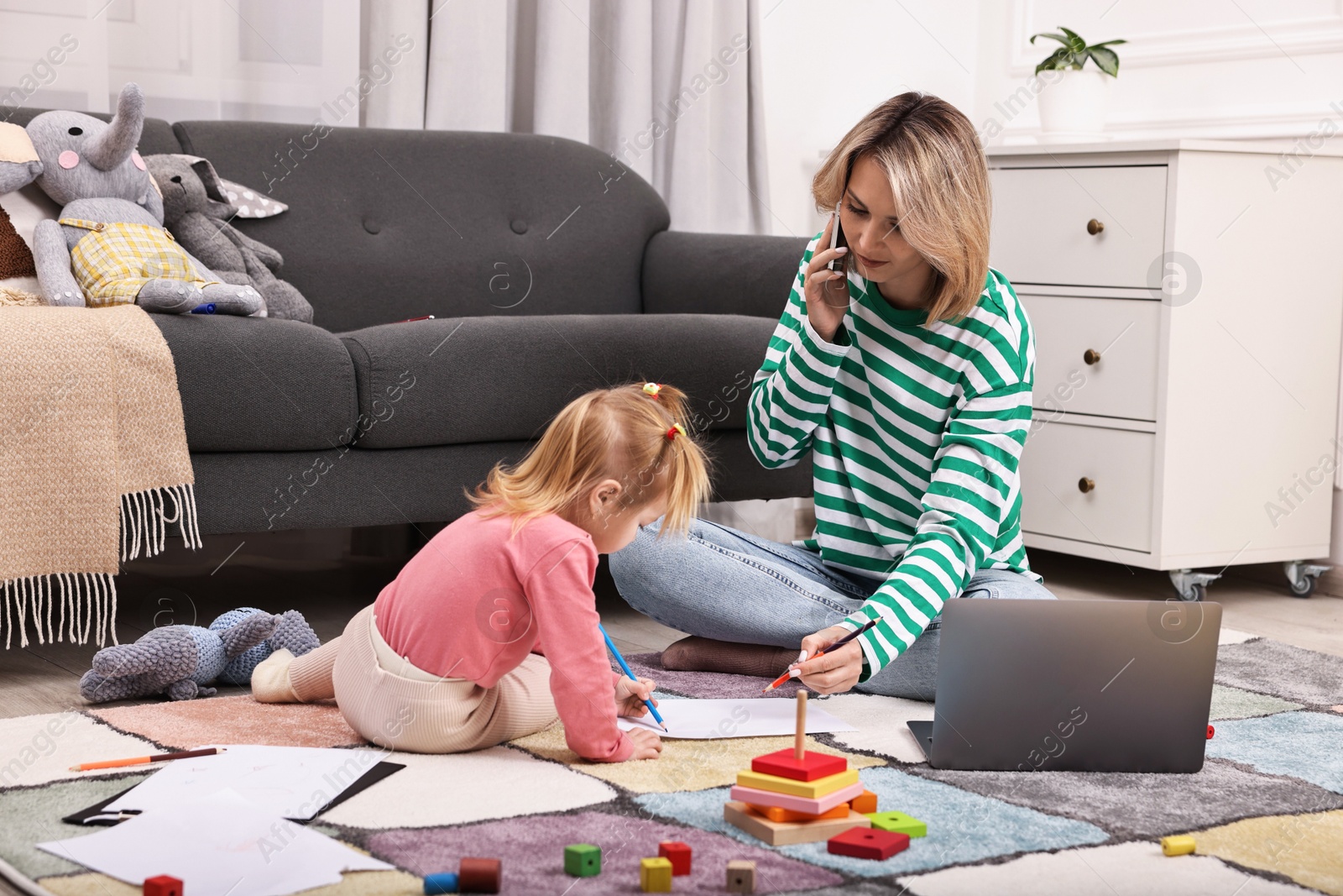 Photo of Work at home. Single mother talking by smartphone and her daughter drawing on floor indoors