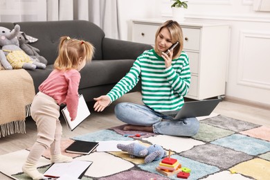 Photo of Work at home. Single mother talking by smartphone and her daughter on floor indoors