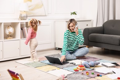 Photo of Work at home. Single mother talking by smartphone and her daughter on floor indoors