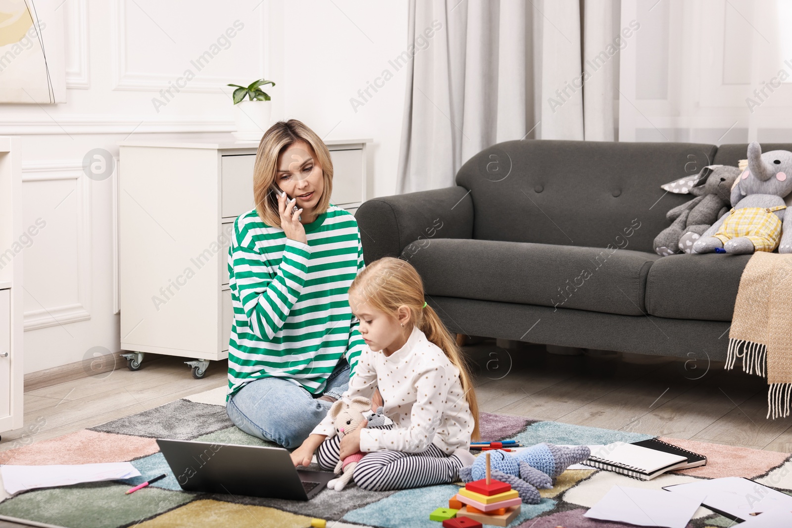 Photo of Work at home. Single mother talking by smartphone and her daughter on floor indoors