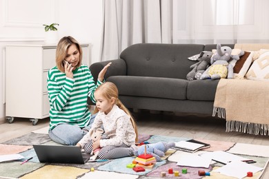 Photo of Work at home. Single mother talking by smartphone and her daughter on floor indoors