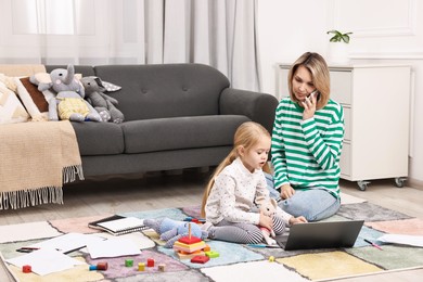 Photo of Work at home. Single mother talking by smartphone and her daughter on floor indoors