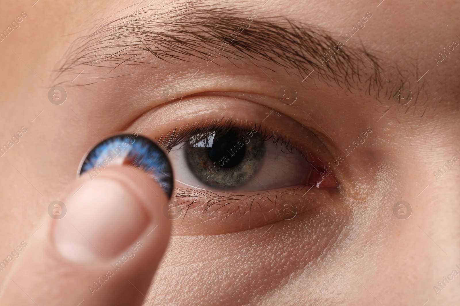 Photo of Man putting color contact lens in his eye, closeup