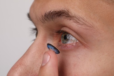 Photo of Man putting color contact lens in his eye on light background, closeup