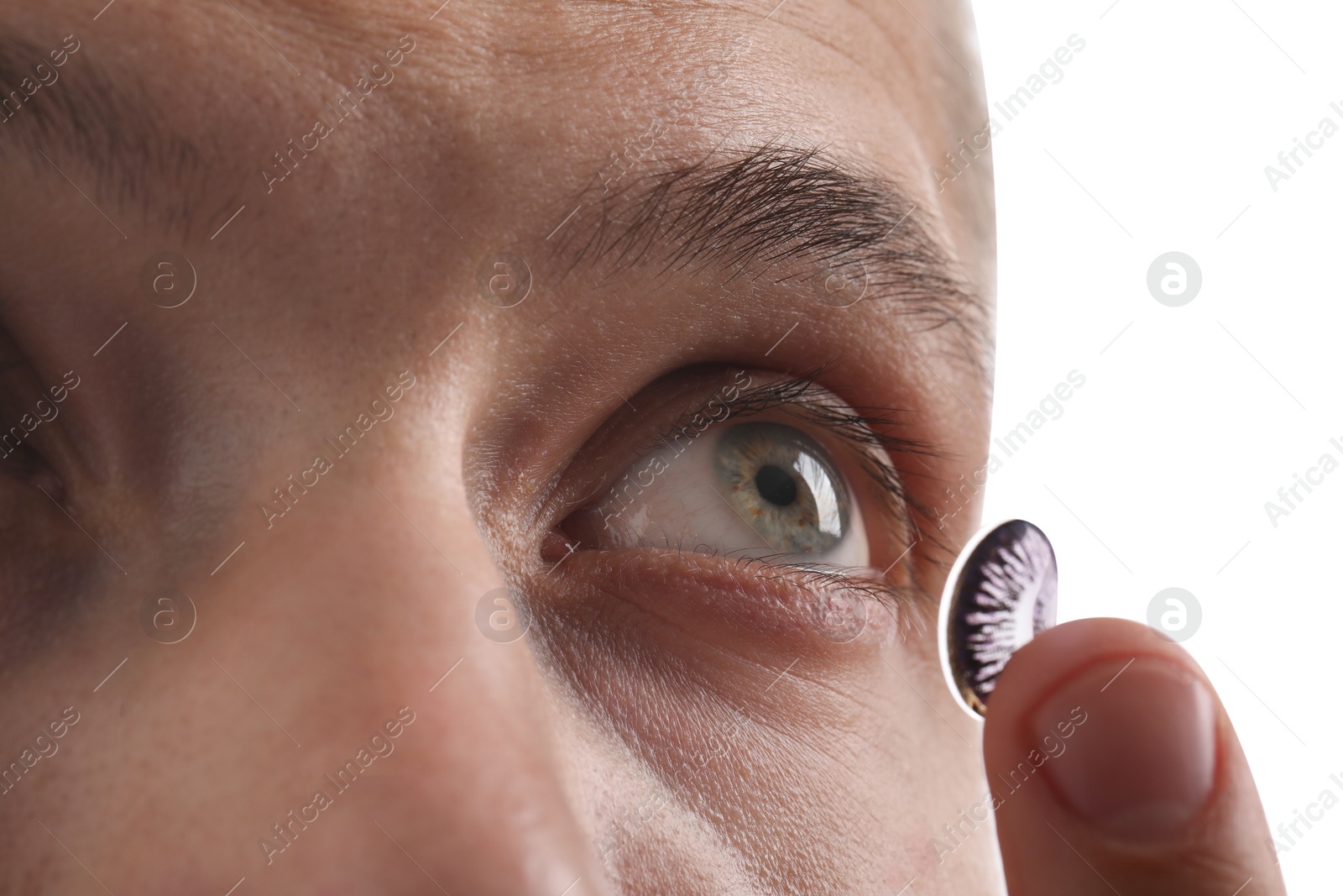 Photo of Man putting color contact lens in his eye on light background, closeup