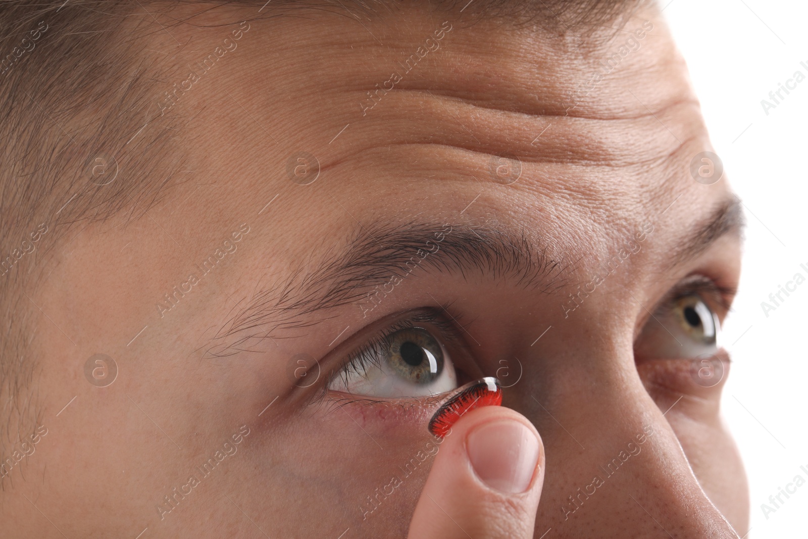 Photo of Man putting color contact lens in his eye on light background, closeup