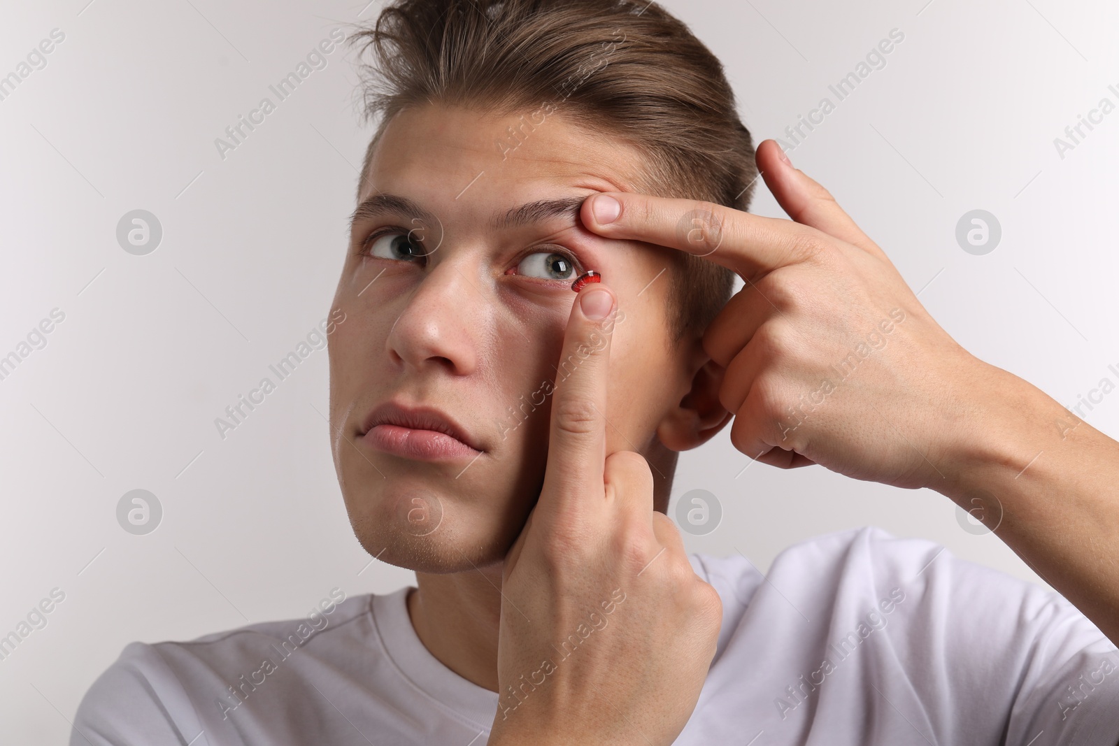 Photo of Man putting color contact lens in his eye on light background