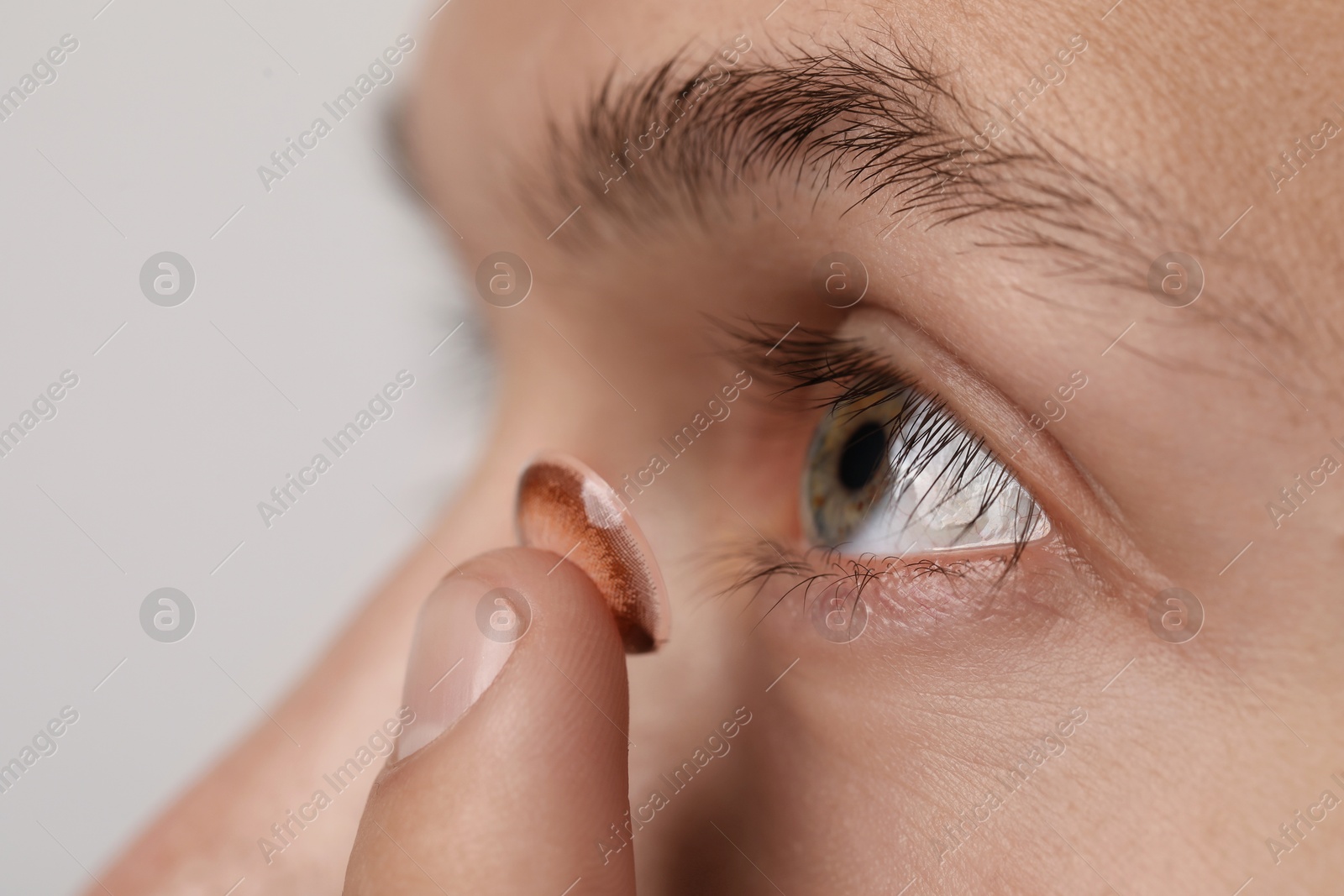 Photo of Man putting color contact lens in his eye on light background, closeup