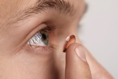 Photo of Man putting color contact lens in his eye on light background, closeup