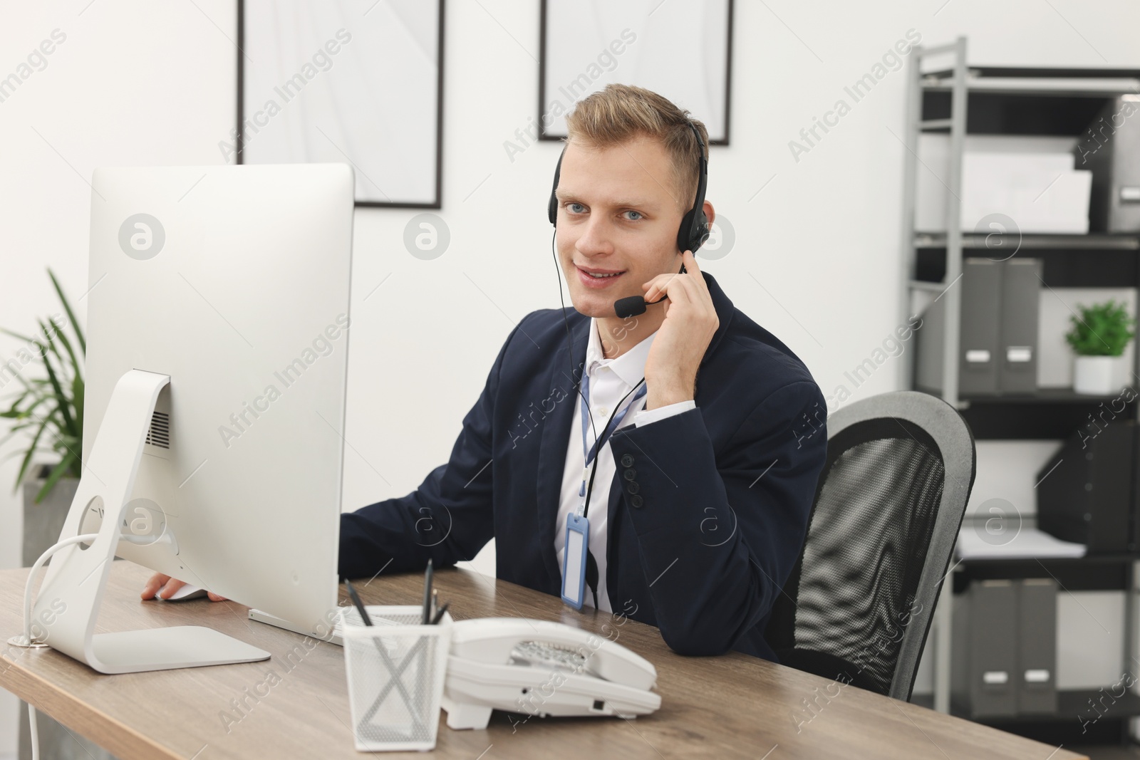 Photo of Technical support call center. Smiling operator working at table in office