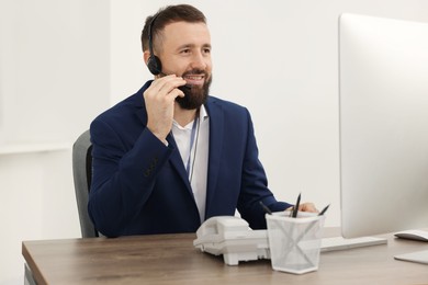 Photo of Technical support call center. Smiling operator working at table in office