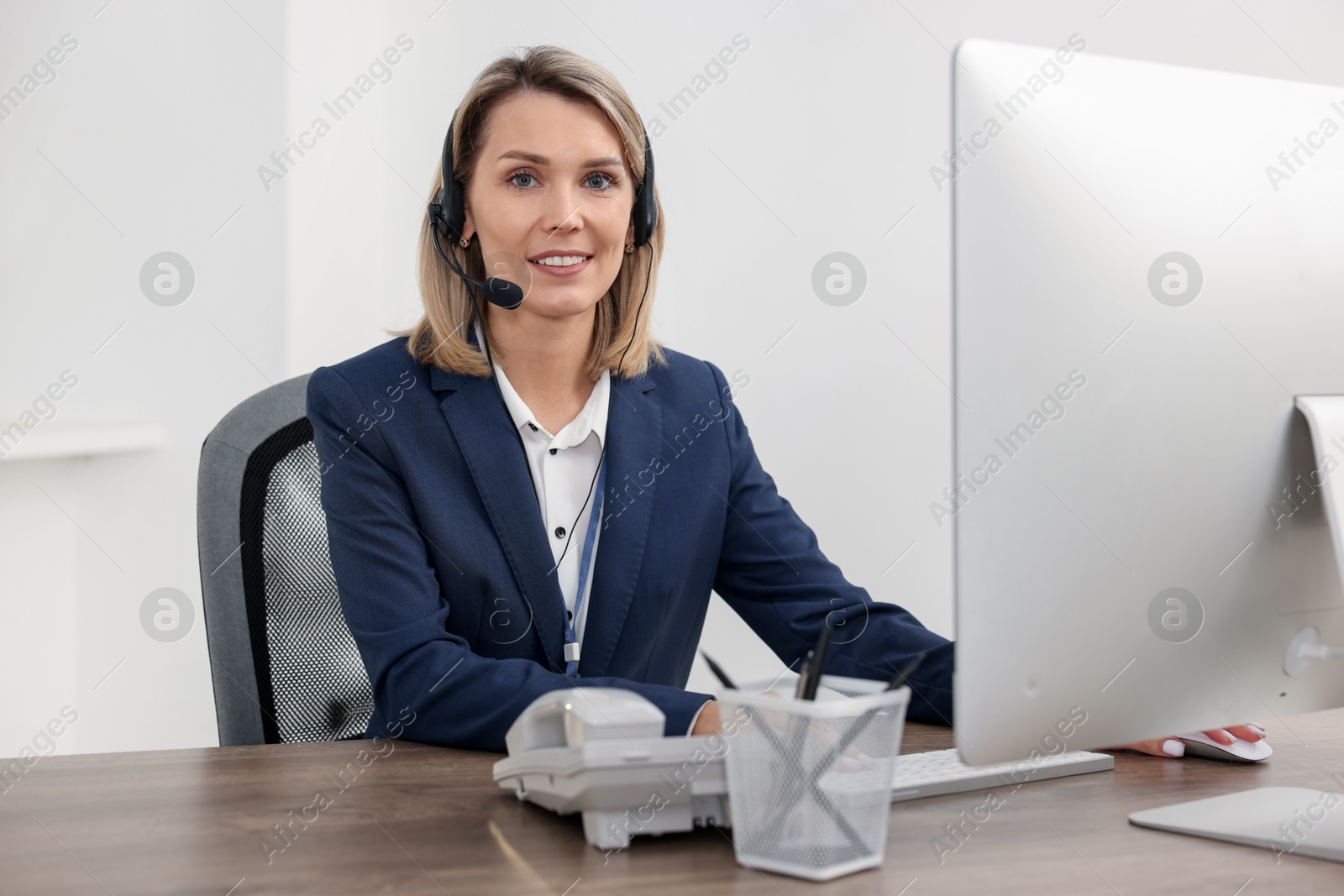 Photo of Technical support call center. Smiling operator working at table in office