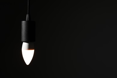 Photo of Glowing light bulb hanging on dark background. Space for text