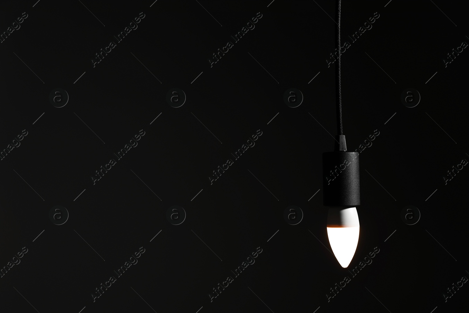 Photo of Glowing light bulb hanging on dark background. Space for text