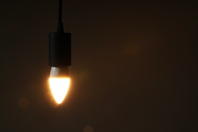 Photo of Glowing light bulb hanging on dark background. Space for text