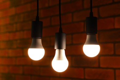 Photo of Glowing light bulbs hanging against brick wall, closeup