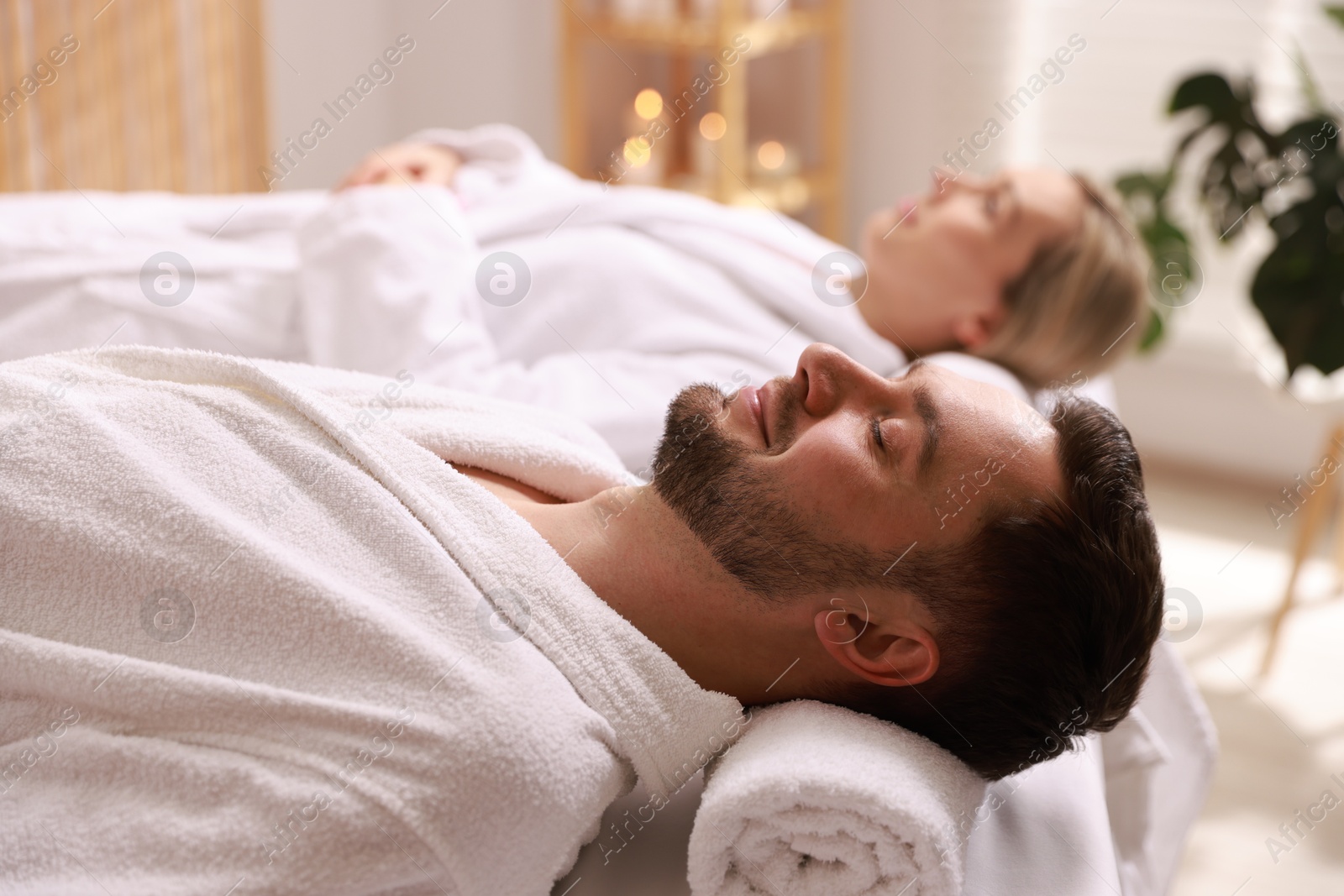 Photo of Couple in bathrobes lying on massage tables in spa salon, selective focus