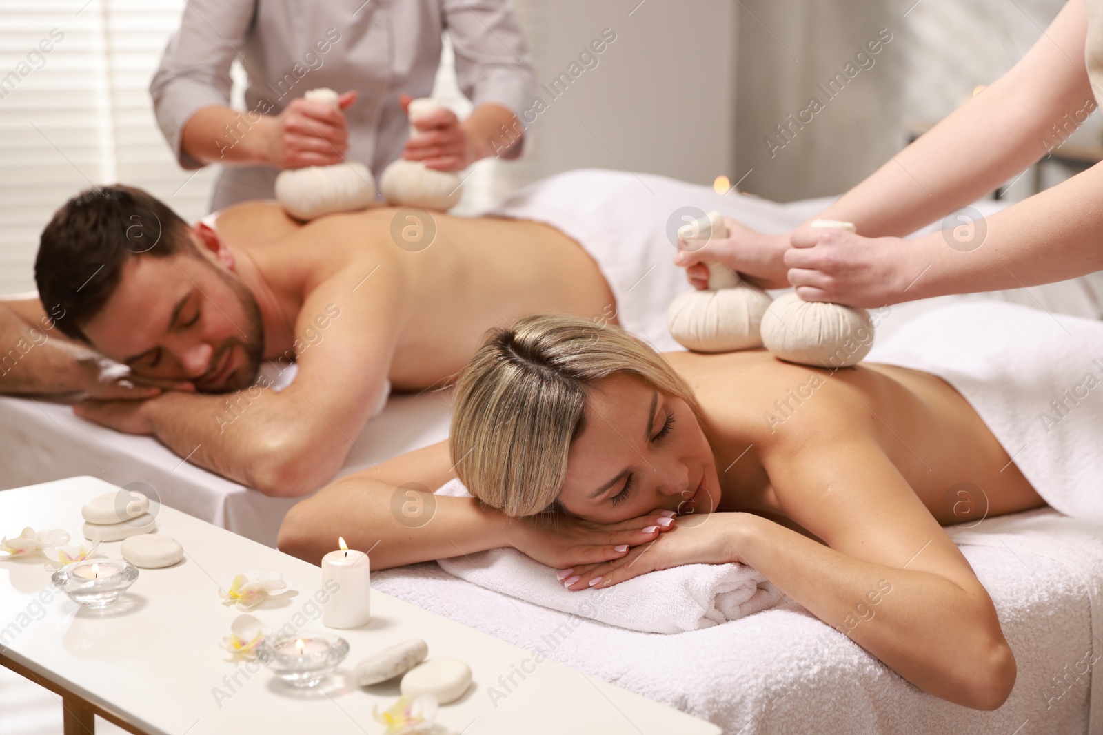 Photo of Couple receiving relaxing massage with herbal bags in spa salon, selective focus