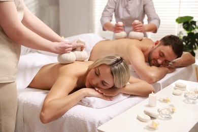 Photo of Couple receiving relaxing massage with herbal bags in spa salon, selective focus