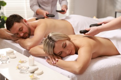 Photo of Couple receiving relaxing massage with stones in spa salon, selective focus