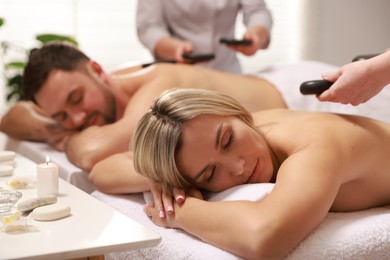 Photo of Couple receiving relaxing massage with stones in spa salon, selective focus