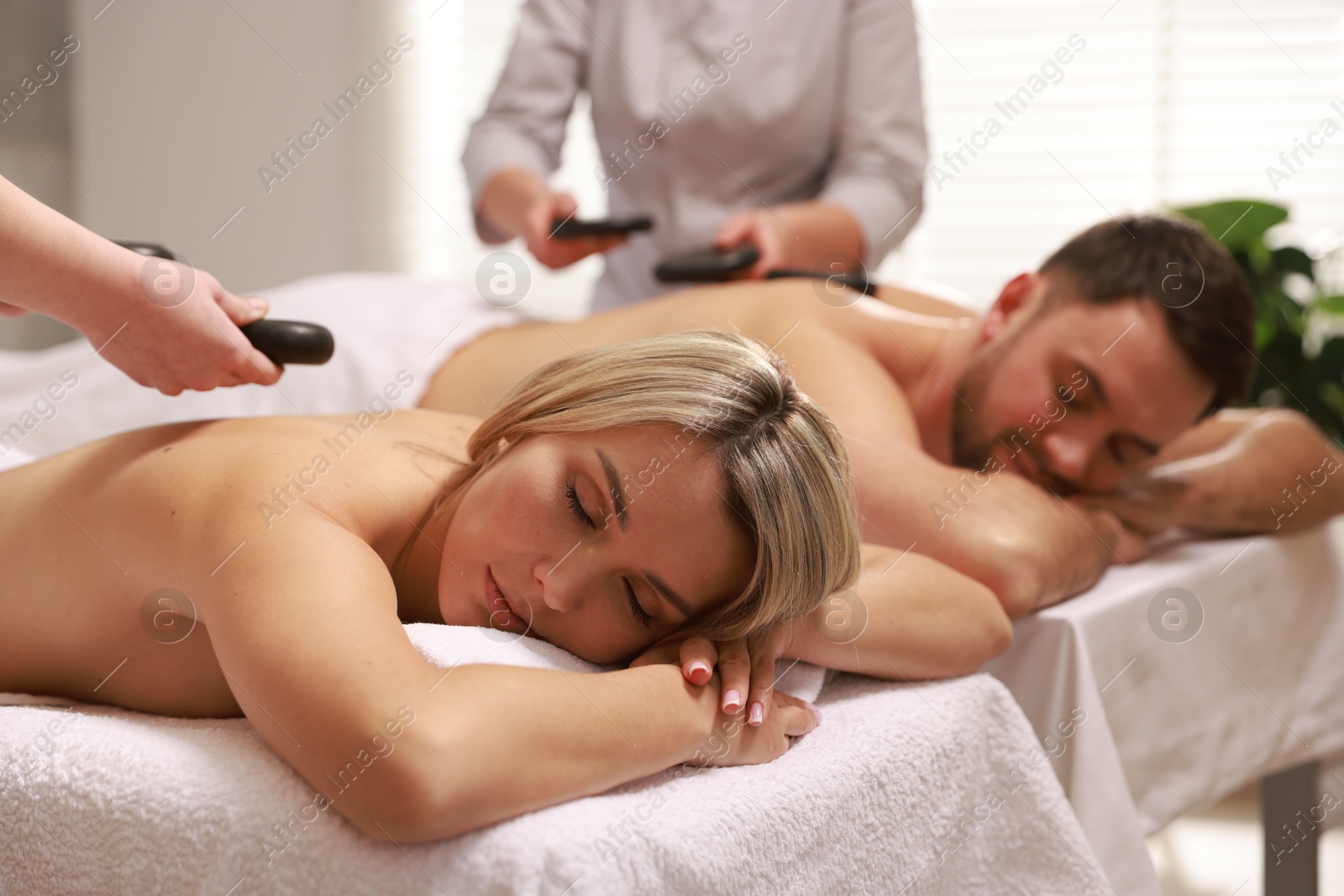 Photo of Couple receiving relaxing massage with stones in spa salon, selective focus