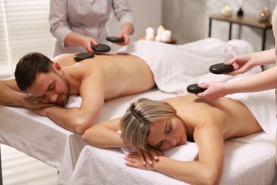 Photo of Couple receiving relaxing massage with stones in spa salon, selective focus