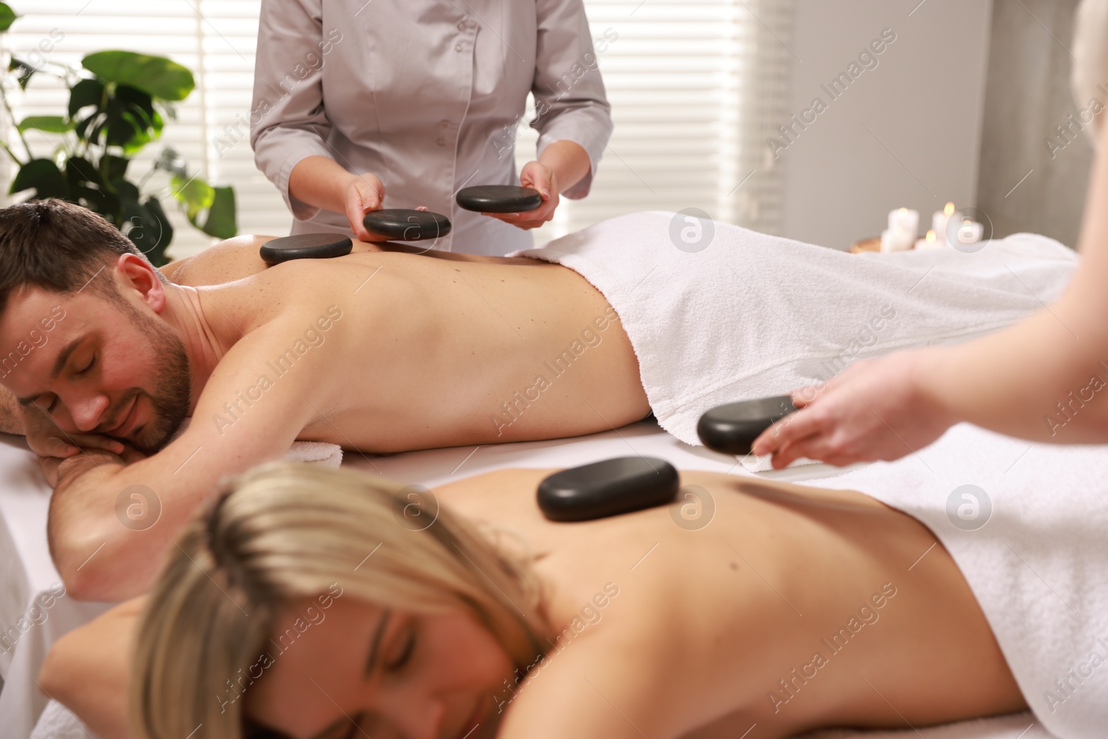 Photo of Couple receiving relaxing massage with stones in spa salon, selective focus