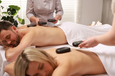 Photo of Couple receiving relaxing massage with stones in spa salon, selective focus