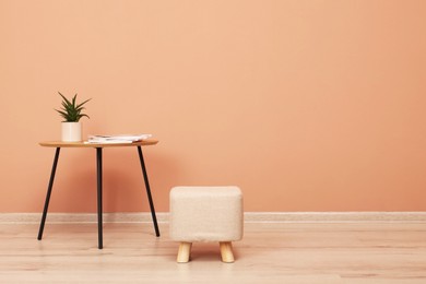 Photo of Comfortable ottoman and table near pale pink wall indoors, space for text