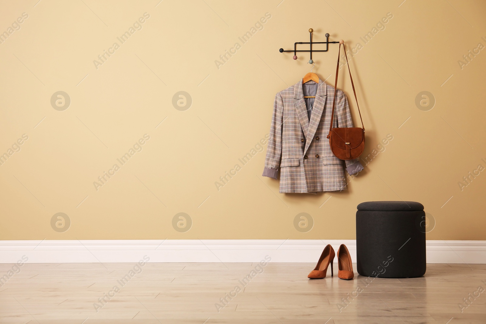 Photo of Stylish comfortable pouf near beige wall in hallway, space for text