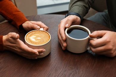 Photo of Colleagues having coffee break at wooden table in cafe, closeup