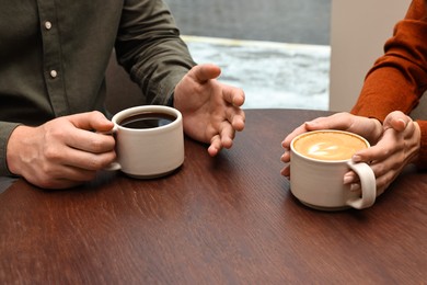 Photo of Colleagues having coffee break at wooden table in cafe, closeup