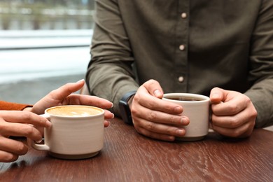 Photo of Colleagues having coffee break at wooden table in cafe, closeup