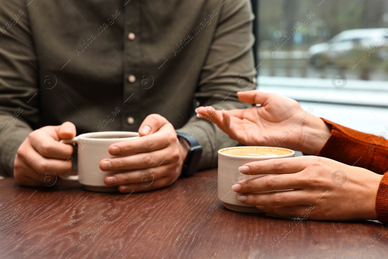 Photo of Colleagues having coffee break at wooden table in cafe, closeup