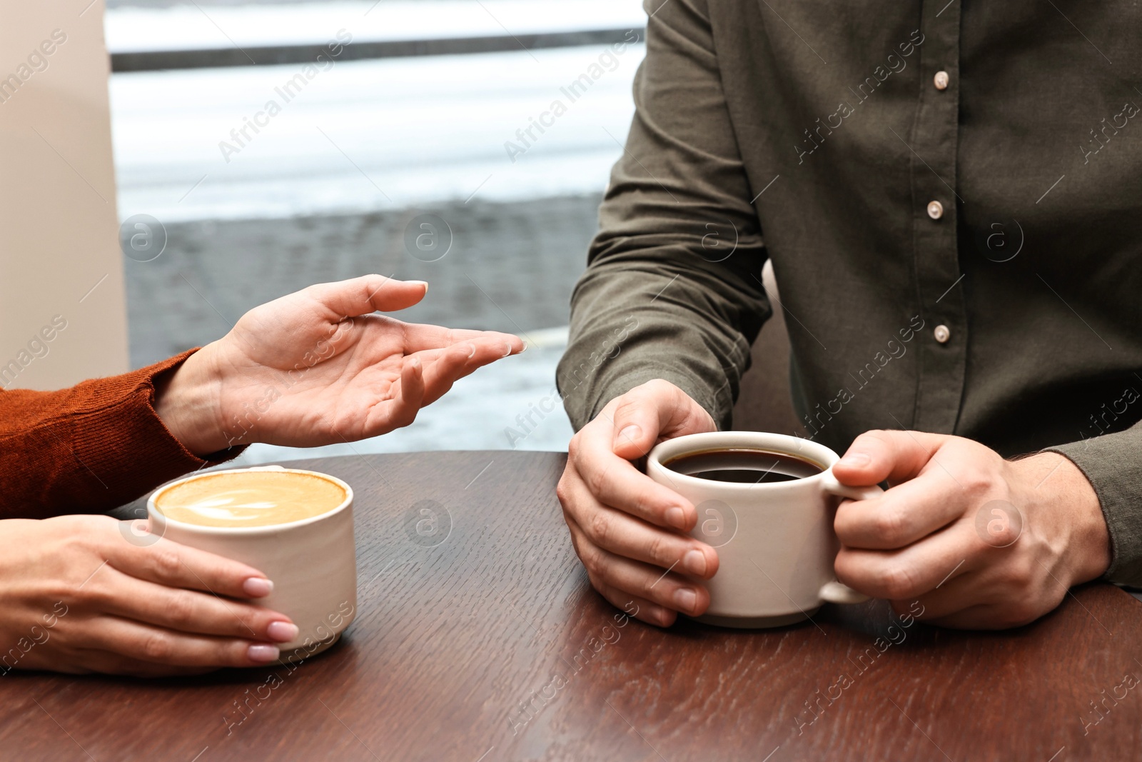 Photo of Colleagues having coffee break at wooden table in cafe, closeup