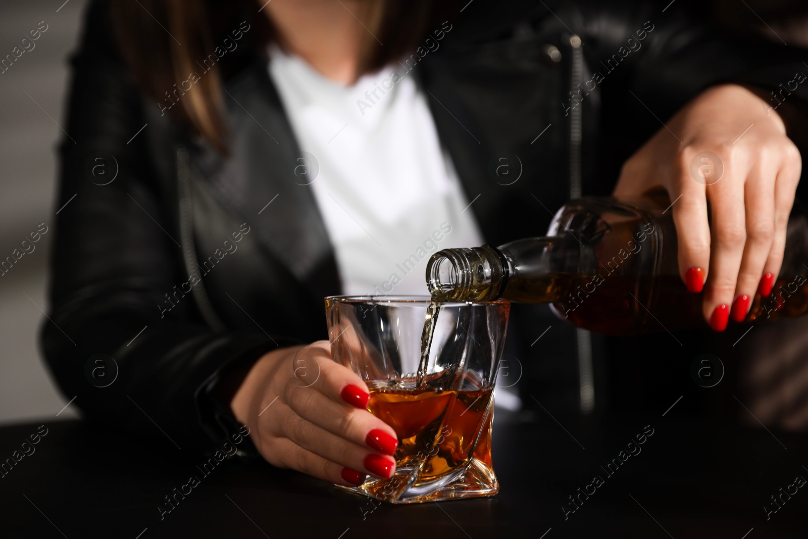 Photo of Alcohol addiction. Woman pouring whiskey into glass at table indoors, closeup