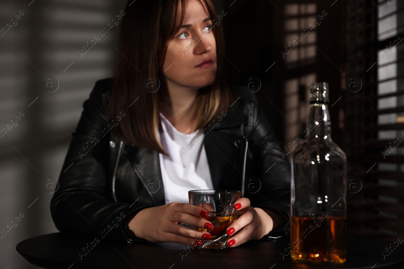 Photo of Alcohol addiction. Woman with glass of whiskey and bottle at table indoors