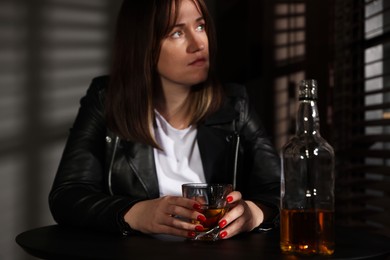 Photo of Alcohol addiction. Woman with glass of whiskey and bottle at table indoors