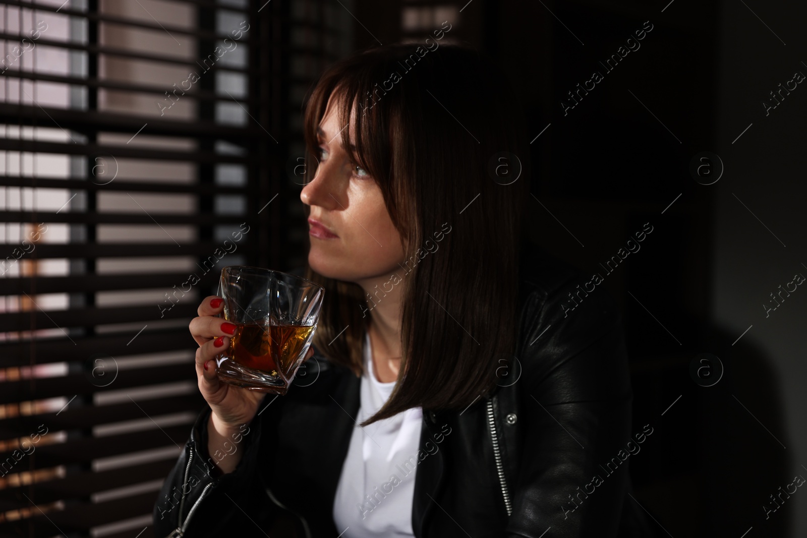 Photo of Alcohol addiction. Woman with glass of whiskey near window indoors