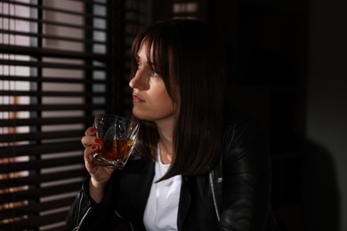 Photo of Alcohol addiction. Woman with glass of whiskey near window indoors