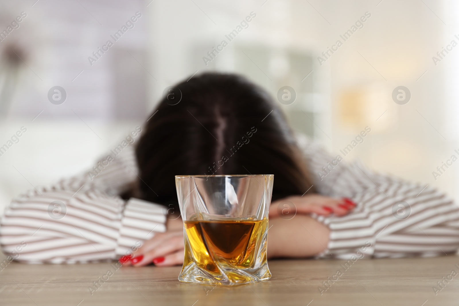 Photo of Alcohol addiction. Woman at wooden table with glass of whiskey indoors, selective focus