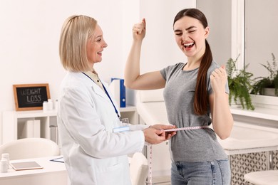 Photo of Happy woman lost weight. Nutritionist measuring patient's waist with tape in clinic