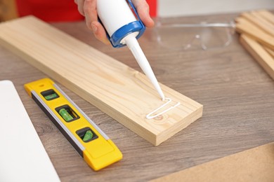 Photo of Man with caulking gun glueing wooden plank at table, closeup